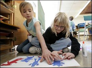 Samantha Merritt, 7, left, offers a helping hand to Kamianna Piekarek, 9, as she glues down a portion of her art project.