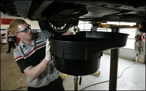 Chris Richardson works on a car at the Tireman in Holland, which charges $16.98 for an oil change 