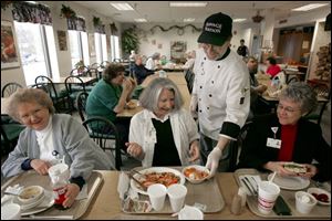 Chef Ray Hohman delivers a dessert of flaming pears to Linda Barbour, center, dining with friends Gloria Instone, left, and Shirley Pickering at Wood County Hospital.