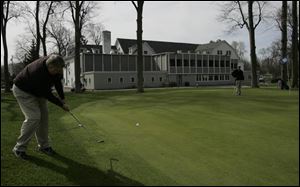 Mike Stark chips onto the green at the ninth hole at Heather Downs Country Club with the clubhouse as the backdrop.


