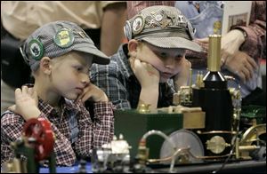 Young engineering hobbyists Robert Taylor, 7, left, and his brother, Nicholas, 9, sport a variety of identifier badges on their caps as they intently watch a model steam engine.