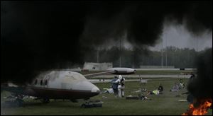 A pall of black smoke from diesel fires lends authenticity to this aircraft disaster drill at Toledo Express Airport. Rescue workers aid 'survivors' of a mock crash on the grass near a runway.