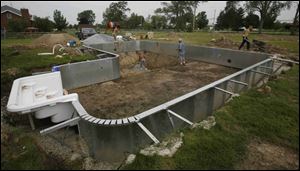 Workers install a pool at Perrysburg home. Despite a tight economy, area pool builders say they are swimming in profits.