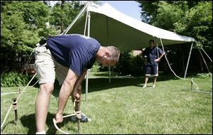 Patrick Kilby, foreground, and Jason Kurtz secure the graduation-party tent's guide ropes.