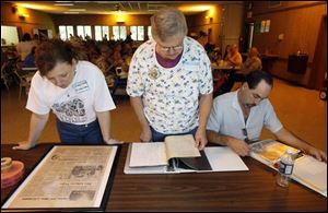 At Ruihley Park Pavilion in Archbold, Ohio, Judy Viers Hinkelman, left, Nancy Henry, and Todd Dixon look at family history collected from 100 years of Viers family reunions.