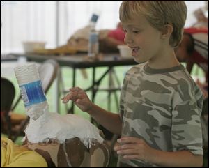 Hannah Pence, 6, of Adrian, finishes the papier-mache mask of Isabel Cueto, 7, of Blissfield, in an effort to emulate a sculpture by Venezuelan artist Marisol. The program has drawn 48 students from the area.