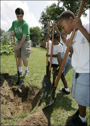 Joe McNamara, candidate for Toledo City Council, digs a hole at the Glenwood Community Garden with the help of, from left, My'Azha Mays, 7, Lavelle Marshall, 7, and Lavaughn Marshall, 6.