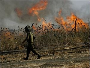 An Israeli soldier walks past a fire surrounding an artillery range after a Hezbollah rocket barrage struck the area near Kiryat Shmona.