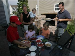 Chip Marlowe prepares to serve pizza baked in the family's pizza oven in Monclova Township. Helping to add toppings are, from left in foreground, T.J. Lee, 10; Mackenzie Marlowe, 3; and Gabby Lee, 7, and in background, Heather Marlowe and the Marlowes' son, Charlie, 8 months.