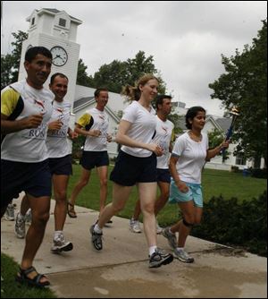 Shyisti Upreti of Nepal carries the torch with fellow runner Sarah Summons, center, of Perrysburg on the campus of Maumee Valley Country Day School. The two women are with team members of the USA World Harmony Runwho stopped in Toledo yesterday during their coast-to-coast mission to promote world peace and harmony.