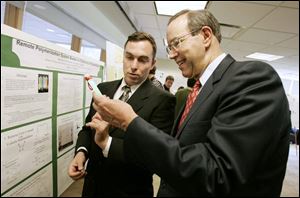 Gov. Bob Taft, right, and Andrei Federov, technical director of the Wright Photoscience Lab at Bowling Green State University, examine a commercially available lightstick that affects polymeric coatings. Mr. Taft announced awards to BGSU's photochemical sciences program. 