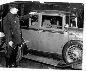 An offi cer points to one bullet hole from the many slugs that hit Jack Kennedy s Pontiac coupe   and Louise Bell   in 1932.
