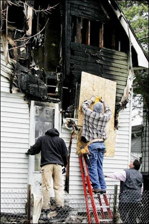 City of Toledo workers Chris O'Larry, left and Stan Harris board up the house at 814 St. John Ave. where four people died in a fire. A suspect was charged in their deaths yesterday.