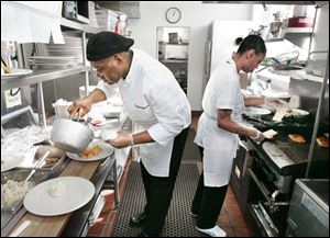 Executive Chef Chris Bates finishes a plate in the kitchen as trainee Tonya Williams cooks.