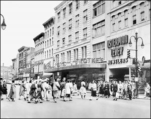 In the 1953 photograph, a crowd of shoppers is
coming and going across the intersection of Adams and
Summit Streets.