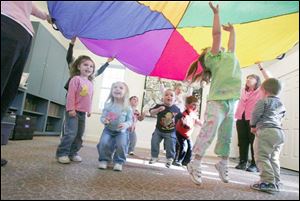 Grace Ermie, 4, jumps up to touch the parachute as, from left, Laura Griffioen, 4, Ella Griffioen, 3, Luke Ermie, 2, Alex Perez, 3, eacher Elaine Sneider, and Adrew Crouse, 2, with his back to the camera, look on.