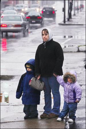 Slug: ROV weather11p        Date:   4/11/2007          The Blade/Amy E. Voigt       Location: Toledo, OH Caption: Charlena Dukett, center, clasps her children J'Shawn Brown, 3, left, and Jaeda Brown, 1, right, while waiting for the bus in the cold and rain. Dukett said that she had been waiting for a bus on Broadway for almost 25 minutes. 