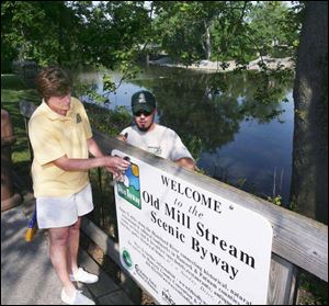 Riverside Park Visual Services Manager Margie Stateler
and Daniel Lamb of park service maintenance attach an
Old Mill Stream Scenic Byway sign to a railing in Findlay.
