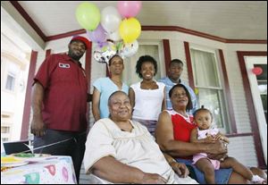 Birthday girl Allissa Scott, top, gets a hug from Thelma Foard, 79, at her Putnam Street home. Above, at back, Robert Smith, Brenda Smith, Britnay Slay, and Allissa's father, Rob Smith, Jr., surround Ms. Foard and Gloria Johnson, holding Allissa. The blade/amy E. voigt Britnay Slay, 16, puts up the party balloons. As a child, Britnay had to distinguish two grandmothers. Allissa has three.