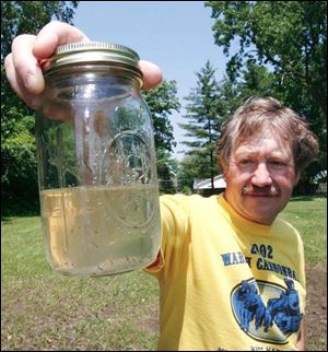 Biologist Lee Mitchell eyes a jar of water containing mosquito larvae that was scooped up near Start High School. Mr. Mitchell says the mosquito crop is early this year.