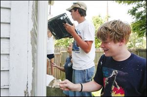 Volunteers Danielle Feeney, Emily Selio, Kody Letterle, and Paul Nagy, from left, keep their paint brushes busy at the back of a home on Kevin Place as part of the Catholic Heart Workcamp efforts. 