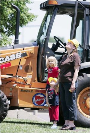Anna Manor, her brother John, and her mother, Shelly Manor, from Southgate, Mich., are on the ground next to a piece of equipment as a crane swings overhead.