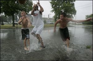 A pickup game of basketball became a wet one of 'waterball' for this trio of North Toledo youngsters after yesterday's rain. Michael Lowry, 13, Emeka Okonkwo, and John Lowry, 14, from left, splash their way through water on Superior Street.