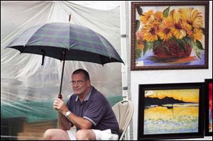 Mike McWilliams, sits under an umbrella outside a booth of artwork created by his wife, local artist Celia McWilliams, during Open Art Days. 