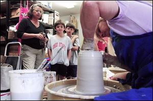Diane Toffler and her grandsons Chad Robertson, center, and Tyler Robertson, watch Toledo Potters Guild member Deb Malinovsky make a piece of pottery.