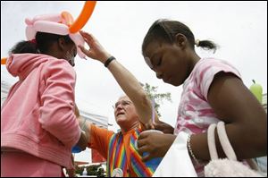 Ashley Stewart, left, gets a helmet from 'Top-O the Balloon Man' as Ashley's sister, Aaliyah Hood, decides to mix her icy drink instead of watching her sister at the street festival.