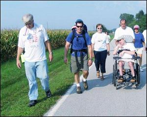 Author Jeff Alt has daughter, Madison, on his back as he walks with stepmother Sue Alt; his father Mike pushes Jeff s brother, Aaron, in a wheelchair, all for the annual Walk with Sunshine.