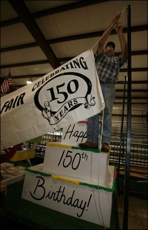 There's no guessing as to which year the fair observes. Richard Mull of Wauseon stands on a cake replica to hang a sign.