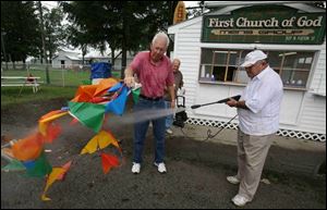 Fran Kieswether of Wauseon, Don Eicher of Delta, and Bill Welch of Wauseon, from left, wash off a banner to get it ready to attract fair visitors to the First Church of God booth. 