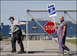 A guard closes a gate at the General Motors plant in Parma, Ohio, as autoworker Anthony Pesce pickets.