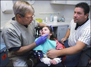 Dentist Jack Whittaker of Bowling Green checks Amber Heiss, 6, of Northwood as her father, Karl, holds her hand. Amber has Rett Syndrome. She uses expressions to communicate.