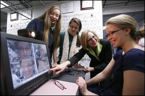Sisters Valeri Wolf, 16, and Rachel Wolf, 13, watch as Mary Nyitray of Optical Arts shows Amelia Wolf, 16.