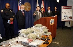 Deputy district attorney Damon Mosler, chief of the narcotics division, center, points out guns and drugs seized during the arrest of 96 people on drug charges at a news conference held in San Diego on Tuesday. 