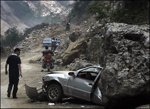 A man looks at a car being half flattened by a huge rock as motorists ride through a damaged road head to Hongkao in Dujiangyan, in southwest China's Sichuan province, Saturday, May 24, 2008. China's earthquake death toll has passed 60,000 and could rise to 80,000 or more, Premier Wen Jiabao said Saturday as he and U.N. Secretary-General Ban Ki-moon visited the disaster area. 