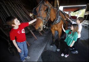 Trevor Lacey, 10, left, and his siblings, Heather, 7, and Trent, 8, pet a horse before going for a carriage ride at Sauder Village, where they were visiting with their parents, Troy and Ruth. The Lacey family is from western Wood County s Bradner.
