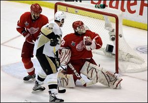 Detroit Red Wings defenseman Andreas Lilja, left, of Sweden, goalie Chris Osgood, right, and Pittsburgh Penguins forward Ryan Malone (12) watch the game-winning goal by Penguins' Petr Sykora during the third overtime period on Tuesday.