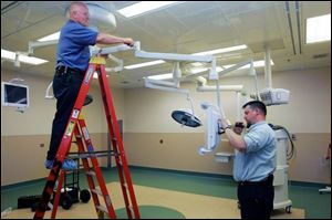 Rich Dusseau, left, and Mike Gilbert, both of Toledo, install monitors and lights in one of the operating rooms.