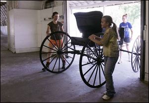 Anthony Wayne Trailblazers 4-H
club members Sarah Matesz, left, Elizabeth Wolf, center, and Valeri Wolf push a 1900s carriage into a
barn for the fair. About seven carriages will be on display and will also be used for horse shows.