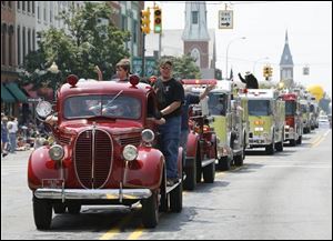 Chris Curson stands on the running board of a 1938 Ida firetruck driven by Cory Jones in a line of fire equipment in yesterday s parade in Monroe to kick off the Monroe County Fair. 