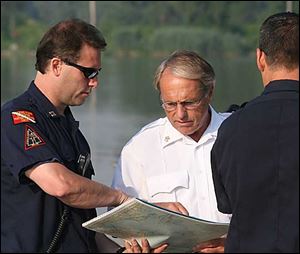 Toledo Fire Chief Mike Wolever, center, looks at a map before rescuers board a boat with a cadaver dog to try and locate the missing father and son.