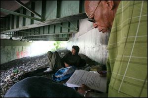 Derick Brown, a homeless National Guard veteran, reclines by his belongings under an overpass near Emerald Avenue in South Toledo as he answers questions from John Whitlow, an outreach worker with Neighborhood Properties Inc. who is part of a team attempting to count the homeless population in Toledo.