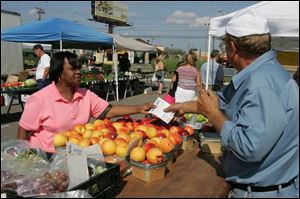 Brenda Slaughter, 64, of Toledo uses vouchers to select fruits and vegetables from Konstadinos Konstandas, also of Toledo, at the Toledo Farmers' Market on Secor Road.