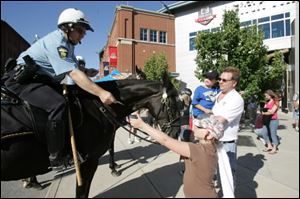 Officer K.E. Bigenho, riding Renegade, gives Brittany Zavac, 9, a trading card picturing himself and his horse as Mark Rosengarten and his grandson, Abel Sanchez, 7, observe.