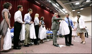 Dr. Ronald McGinnis, center, an associate dean at the University of Toledo college of medicine, formerly the Medical College of Ohio, helps one of 176 new medical students into his doctor s white coat yesterday at the White Coat Ceremony on the UT campus.