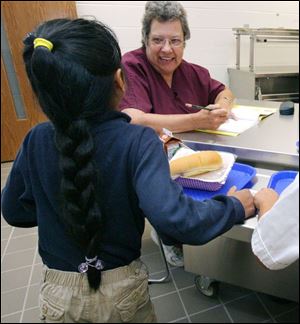 Pat DeMoe, a food server, marks off names of first and second graders taking hot lunch in the cafeteria at Sherman Elementary School during the first day of classes last week. This year, parents with children in the Toledo Public School District are finding it easier for their children to be eligible for free or reduced meals because of new rules in the program.