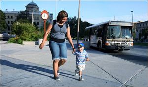 Natasha Mitcham walks her son Keshawn Jones to the bus stop shelter at Huron and Jackson streets. Ms. Mitcham and her son depend on the bus system to reach her job at a day-care center. Twenty of the TARTA bus routes were changed, but printed timetables reflecting the new times have yet to be printed.
